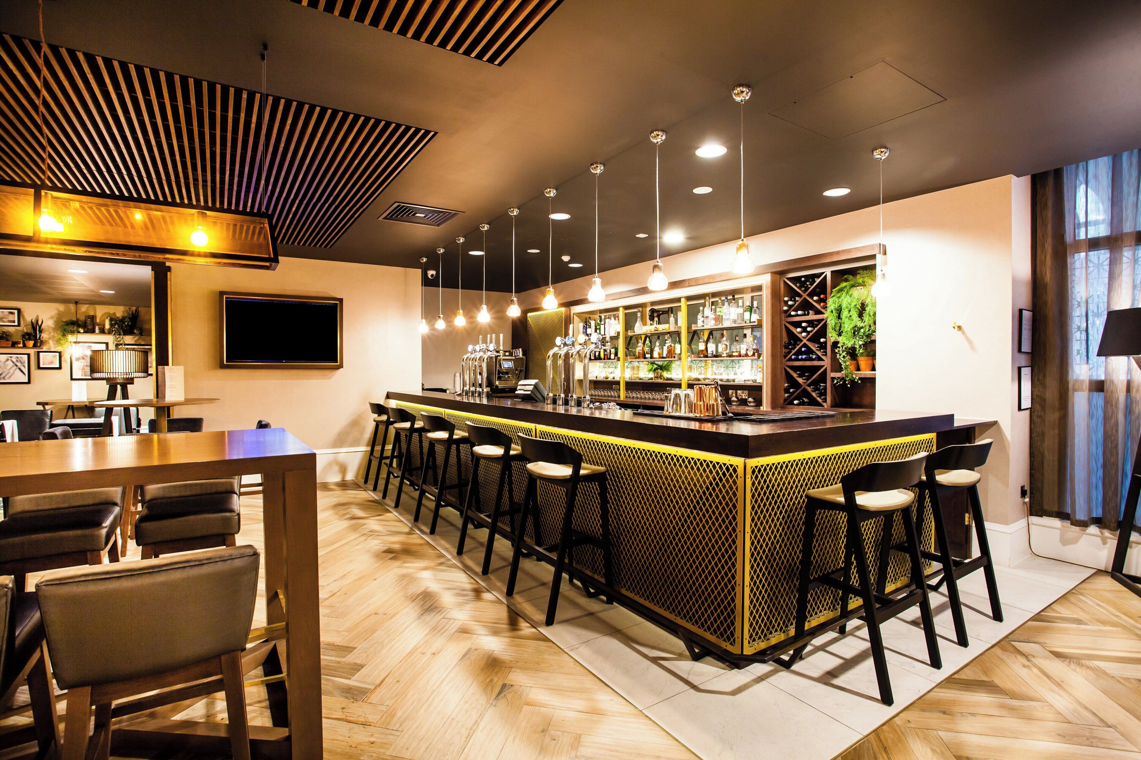 A bar area with a long counter, multiple stools, and a television screen.