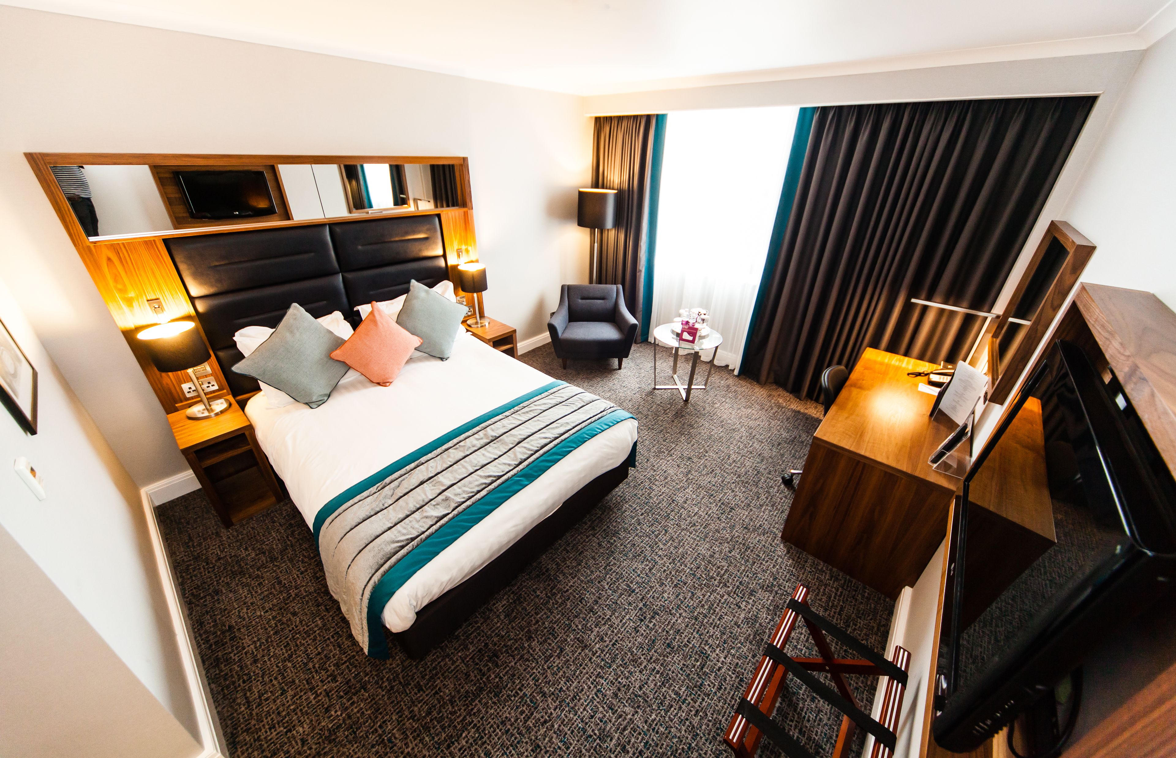 A hotel room with a large bed, a desk, a chair, a TV, and a window with curtains.