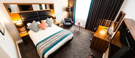 A hotel room with a large bed, a desk, a chair, a TV, and a window with curtains.