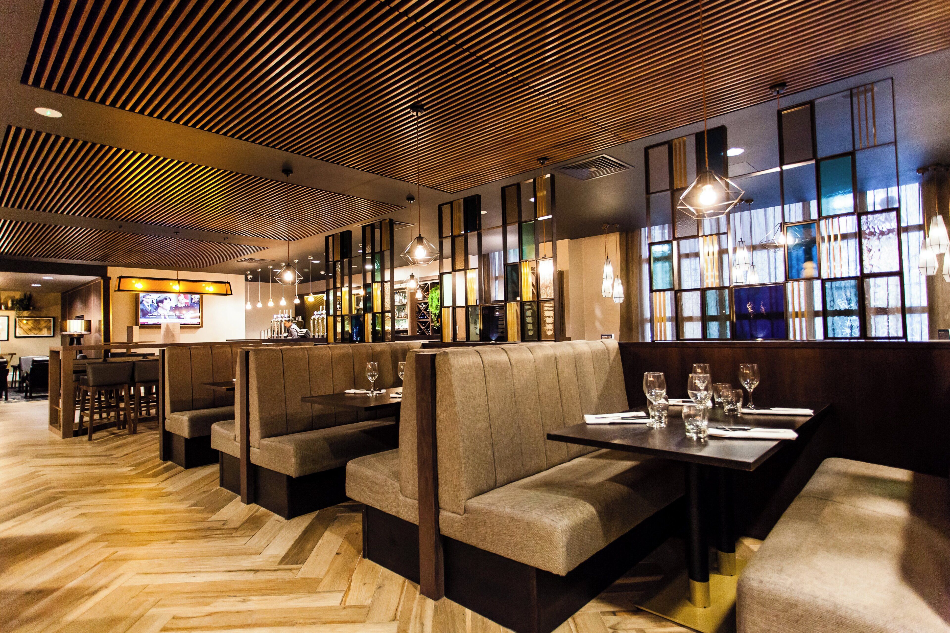 A restaurant interior with booths and tables, wooden flooring, and pendant lighting.