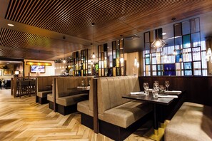 A restaurant interior with booths and tables, wooden flooring, and pendant lighting.