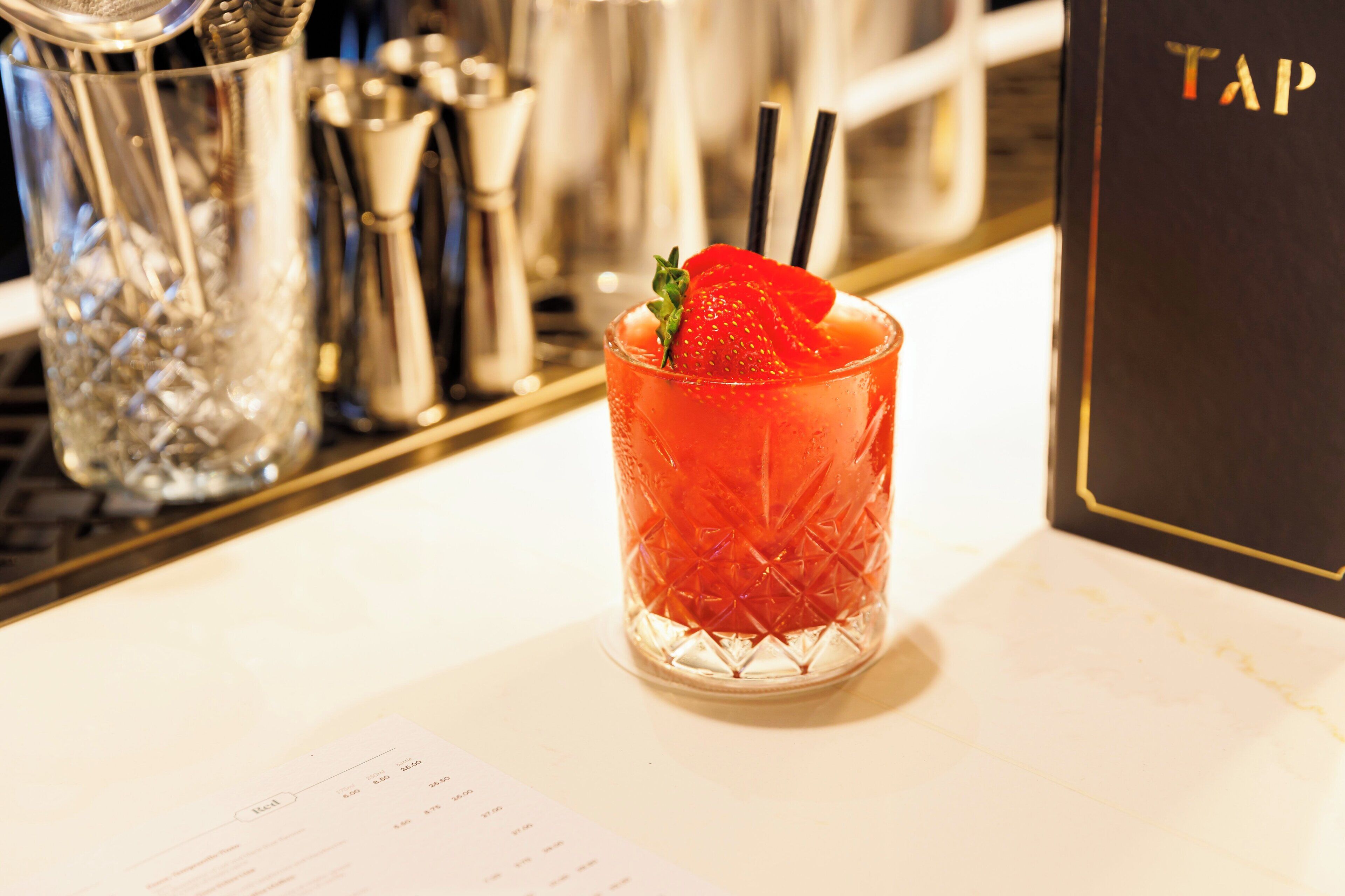 Un verre à cocktail, décoré d’une fraise, posé sur le comptoir d’un bar.