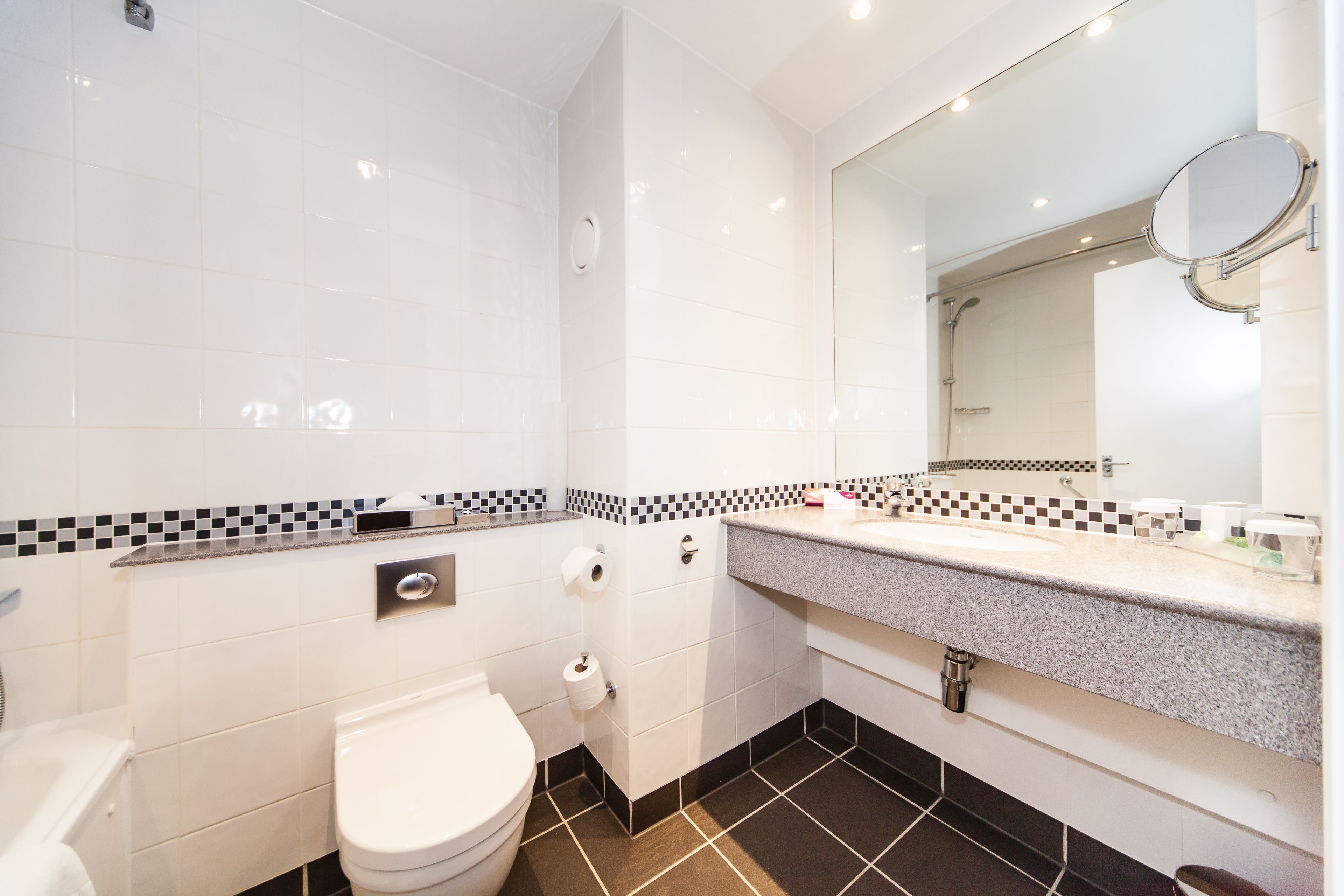 A modern bathroom with white tiles, a black and white checkered backsplash, a white toilet, a sink with a mirror, and a shower area.