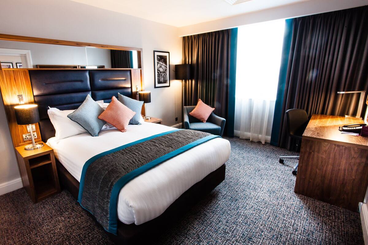 A hotel room with a large bed, a desk, a chair, and a view of the outdoors.