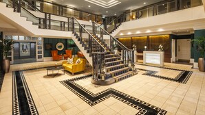 A spacious lobby with a central staircase, a reception desk, and a seating area with a yellow sofa. - Crowne Plaza Leeds by IHG (Leeds)