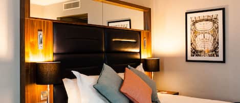Een hotelkamer met een groot bed, een houten hoofdeinde, twee bedlampen en een ingelijste foto aan de muur.