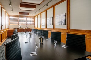 A conference room with a long table, black chairs, and wooden paneling.