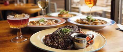 A restaurant setting with a table set for a meal, including a steak, wine glasses, and a cocktail.