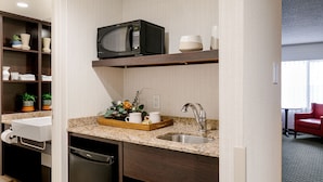 Una cocina compacta con microondas integrado, un lavamanos y una encimera con una cesta de objetos.
