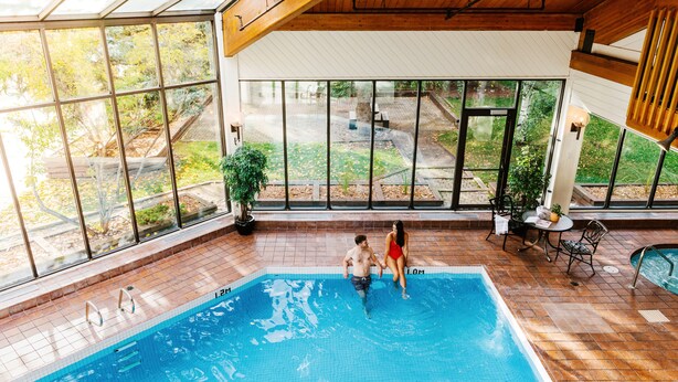 Una piscina interior con paredes de vidrio transparente, suelo de baldosas y vistas al exterior.