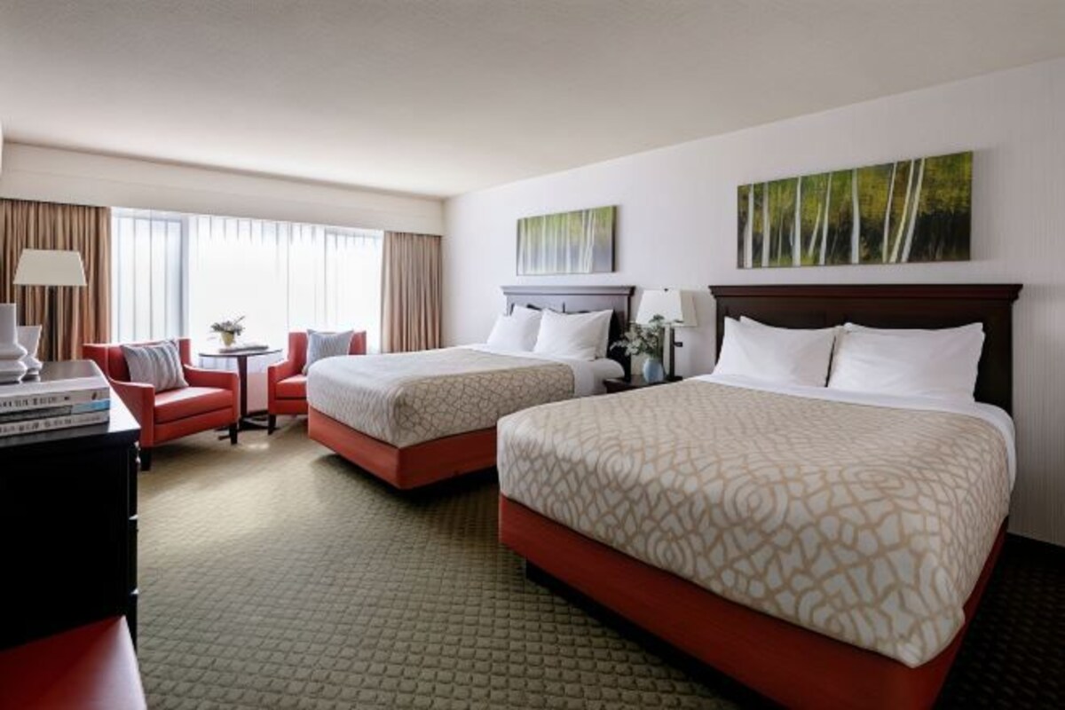 Una habitación de hotel con dos camas, un escritorio, una silla y un ventanal con cortinas.