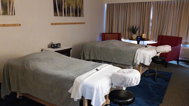A hotel room with two beds, a massage chair, a small table with a plant, and a window with curtains. - Chateau Jasper (Jasper)