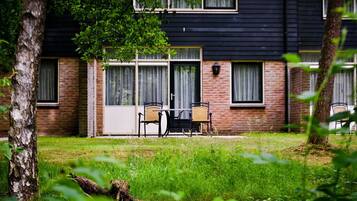 Een gebouw met twee verdiepingen, een bakstenen gevel en grote ramen. Er is een patio met tuinmeubilair.