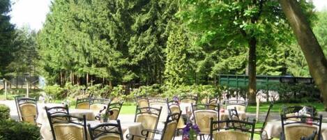 Un espace extérieur aménagé avec des chaises et des tables en osier, entouré d’arbres et de verdure.