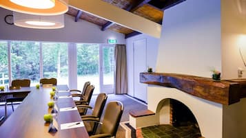 Un salón de conferencias con una mesa larga, sillas, chimenea y grandes ventanales que dan a un paisaje arbolado.