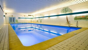 Una piscina interior con suelo y paredes de azulejos, techo con líneas horizontales y un mural de palmeras.