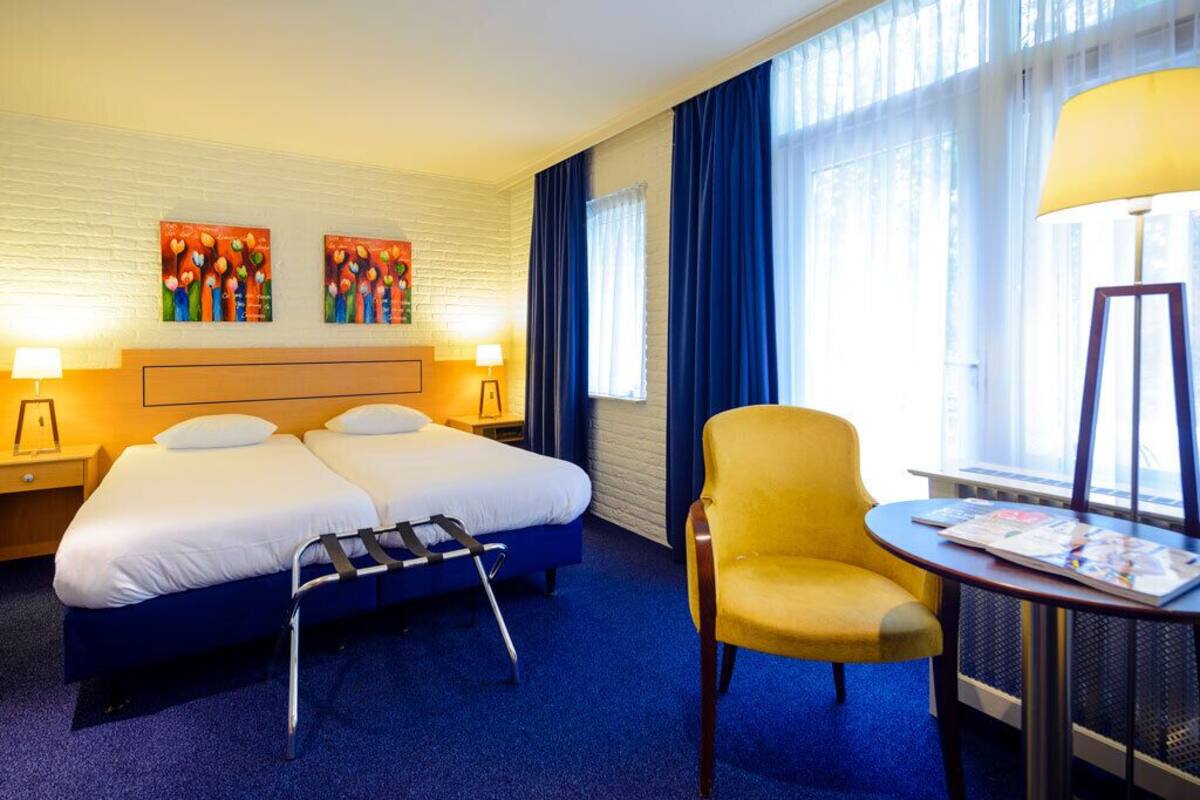 A hotel room with two beds, a chair, a table, and artwork on the wall.