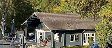 Un petit bâtiment d’un seul étage, doté d’un toit à pignon, probablement un restaurant ou un café, entouré d’arbres et d’un espace de stationnement.