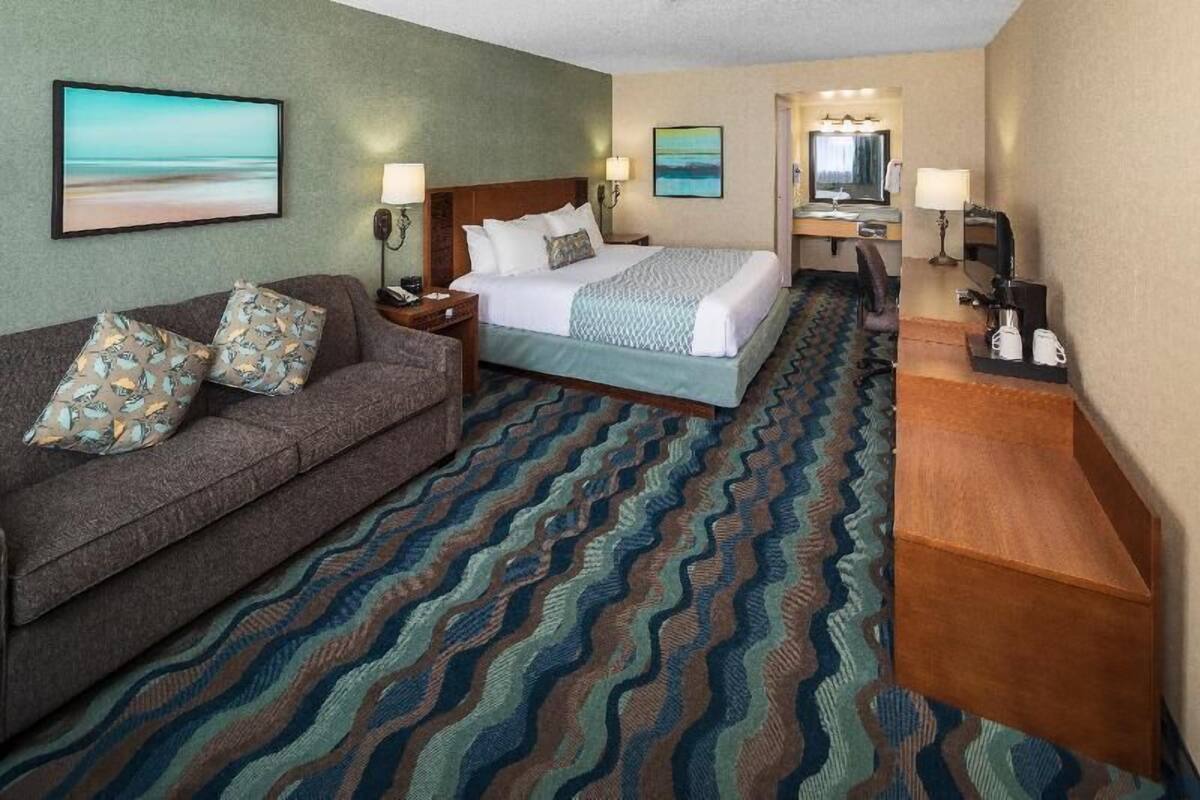 Habitación de hotel con cama, sofá, escritorio y espejo de baño.