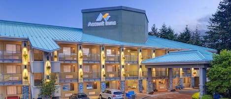 Un hôtel à plusieurs étages, reconnaissable à son grand panneau « Accent Inns », doté de nombreux balcons et disposant d’un parking où sont stationnées plusieurs voitures.