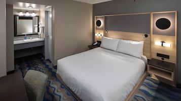 A hotel room with a large bed, a bathroom with a mirror and sink, and a chair.
