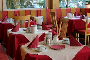 Ein Restaurant mit gedeckten Tischen, mit roten Tischdecken und Holzstühlen.