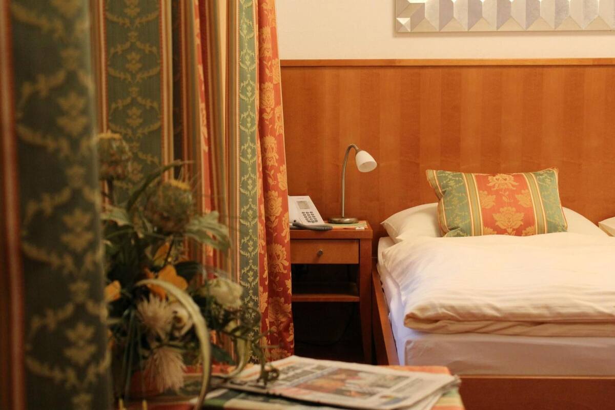 Une chambre d’hôtel avec une tête de lit en bois, une table de chevet avec une lampe, un téléphone et un coussin décoratif.