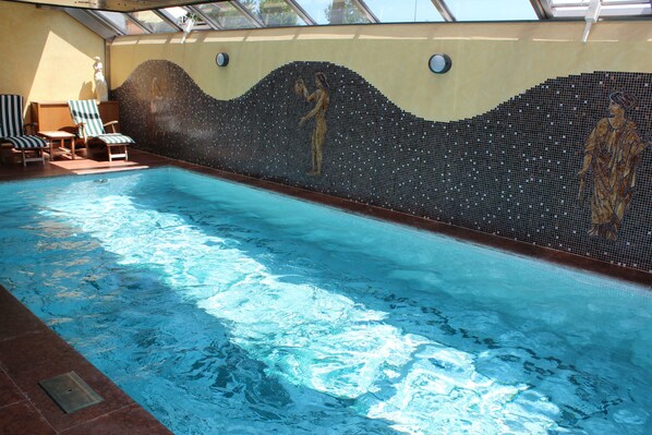 Ein Innenpool mit Mosaik-Wandbildern, Liegestühlen und einem Oberlicht.