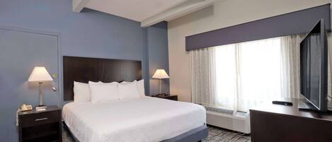 A hotel room with a large bed, two bedside tables with lamps, a TV, and a window with curtains.