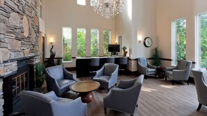 A spacious lobby with a stone wall, a chandelier, multiple seating areas, and large windows offering views of greenery. - Elm Hurst Inn & Spa, WorldHotels Crafted (Ingersoll)