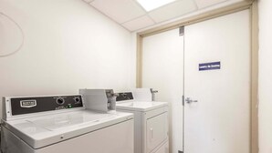 Een wasruimte met een Maytag wasmachine voor commercieel gebruik, een droger en een deur met een bordje 'Wassen - Niet roken'.
