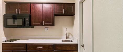 A compact kitchen with dark wooden cabinets, a built-in microwave, and a stainless steel sink.