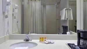 Een hotelbadkamer met een wastafel, spiegel, handdoekhouder en een koffiezetapparaat.