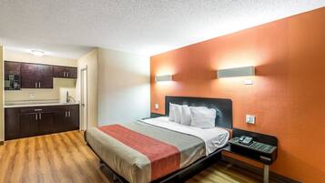 A hotel room with a bed, a bedside table with a phone, a microwave in the kitchenette, and a bathroom door.