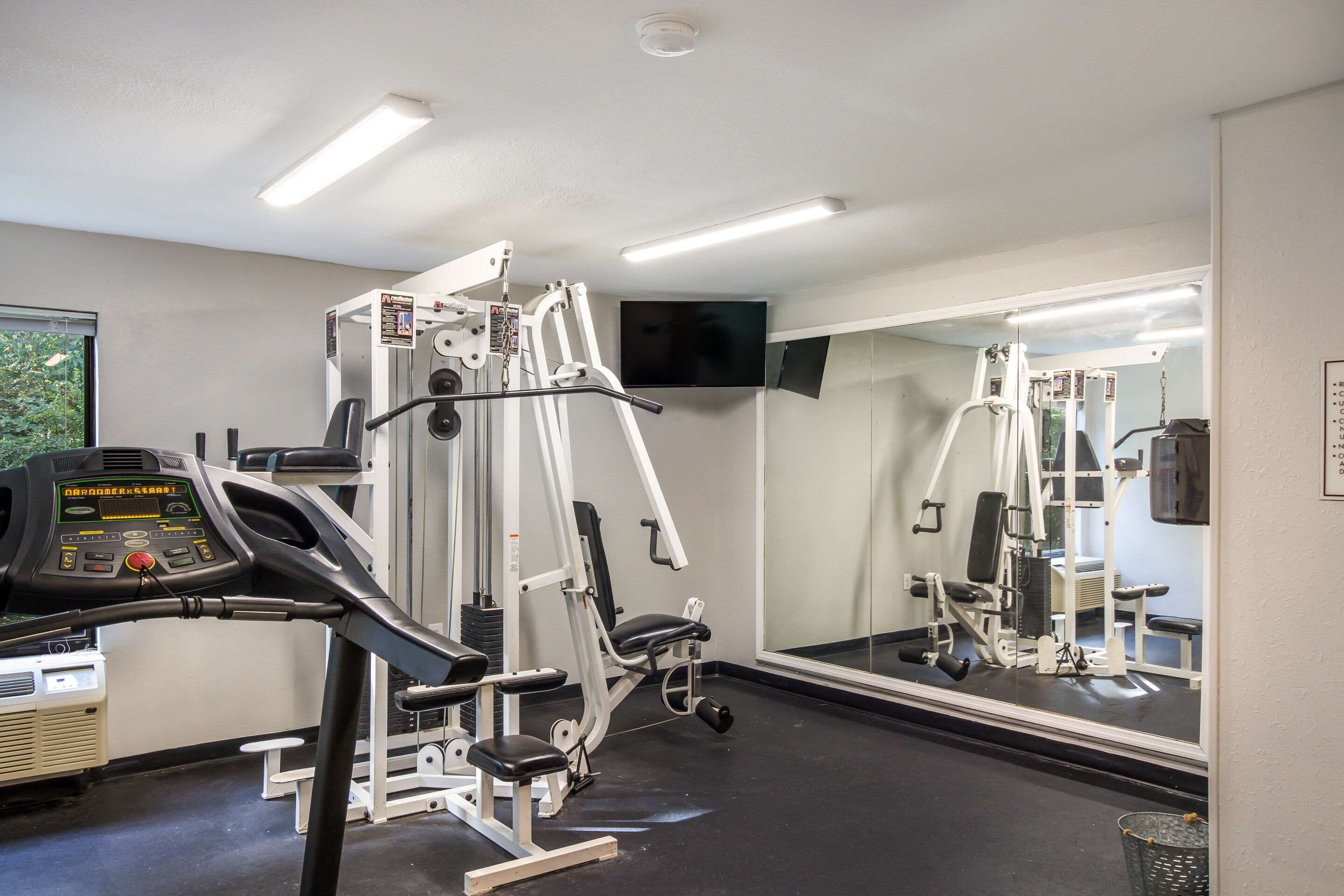 Un gimnasio con equipo de ejercicio, cinta de correr y un espejo grande.