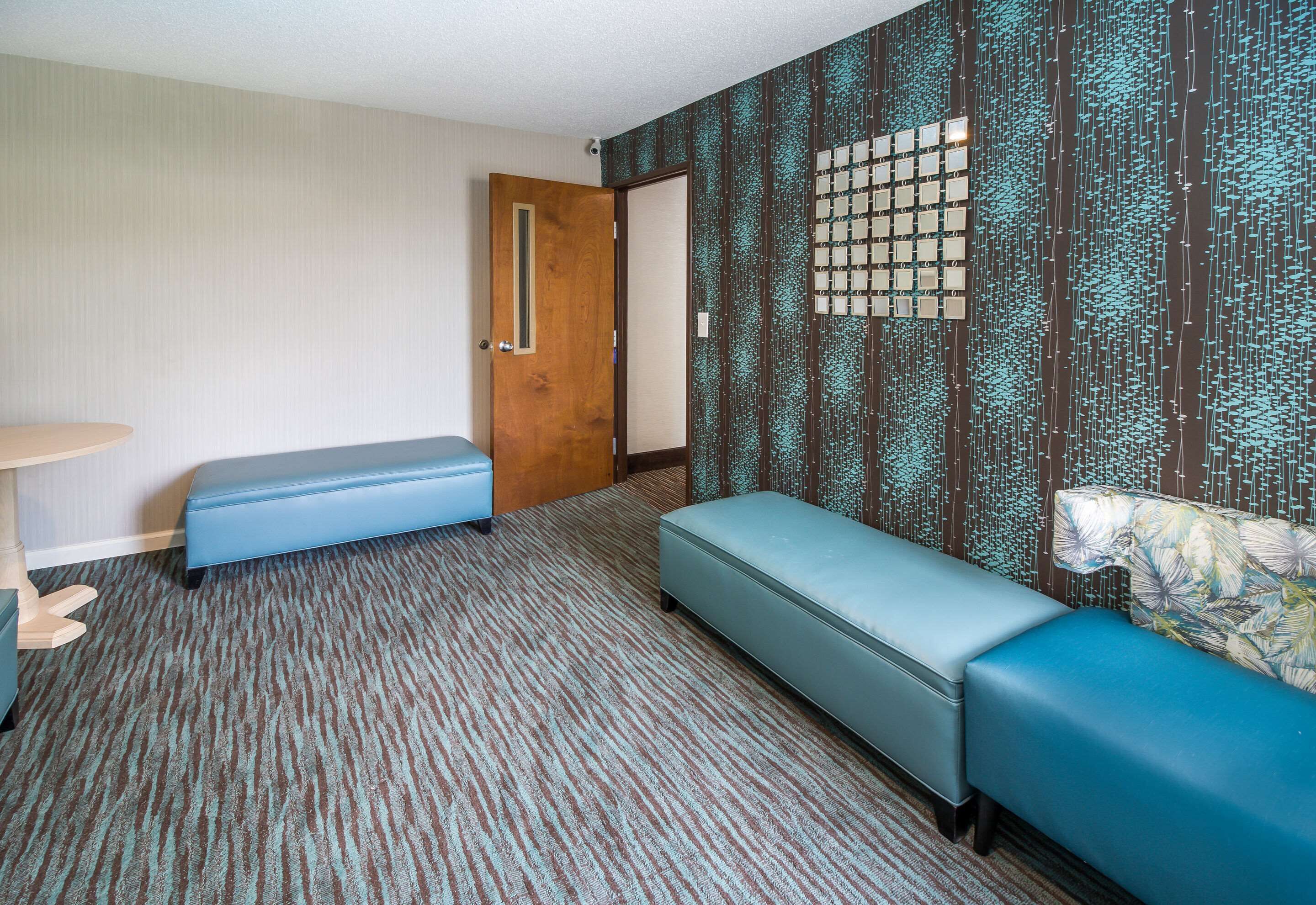 A room with a patterned carpet, a wooden door, a bench, a small table, and a patterned wall.