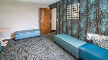 A room with a patterned carpet, a wooden door, a bench, a small table, and a patterned wall.