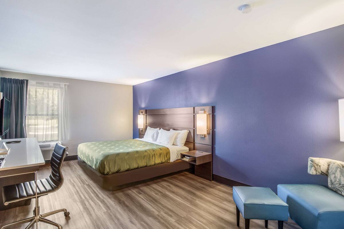 Une chambre d’hôtel comprenant un lit, un bureau, une chaise et deux poufs.