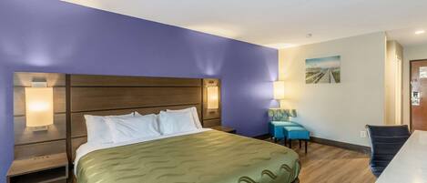 Ein Hotelzimmer mit einem großen Bett, einem Nachttisch, einem Schreibtisch und einem Sessel.