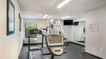 Un gimnasio con cintas de correr, escaladora y un espejo grande.