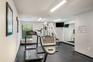 Un gimnasio con cintas de correr, escaladora y un espejo grande.