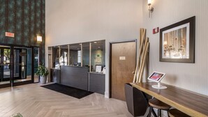A hotel reception area with a herringbone wood floor, a reception desk with a digital screen, and a framed artwork on the wall. - Quality Inn near MCAS Cherry Point (Havelock)