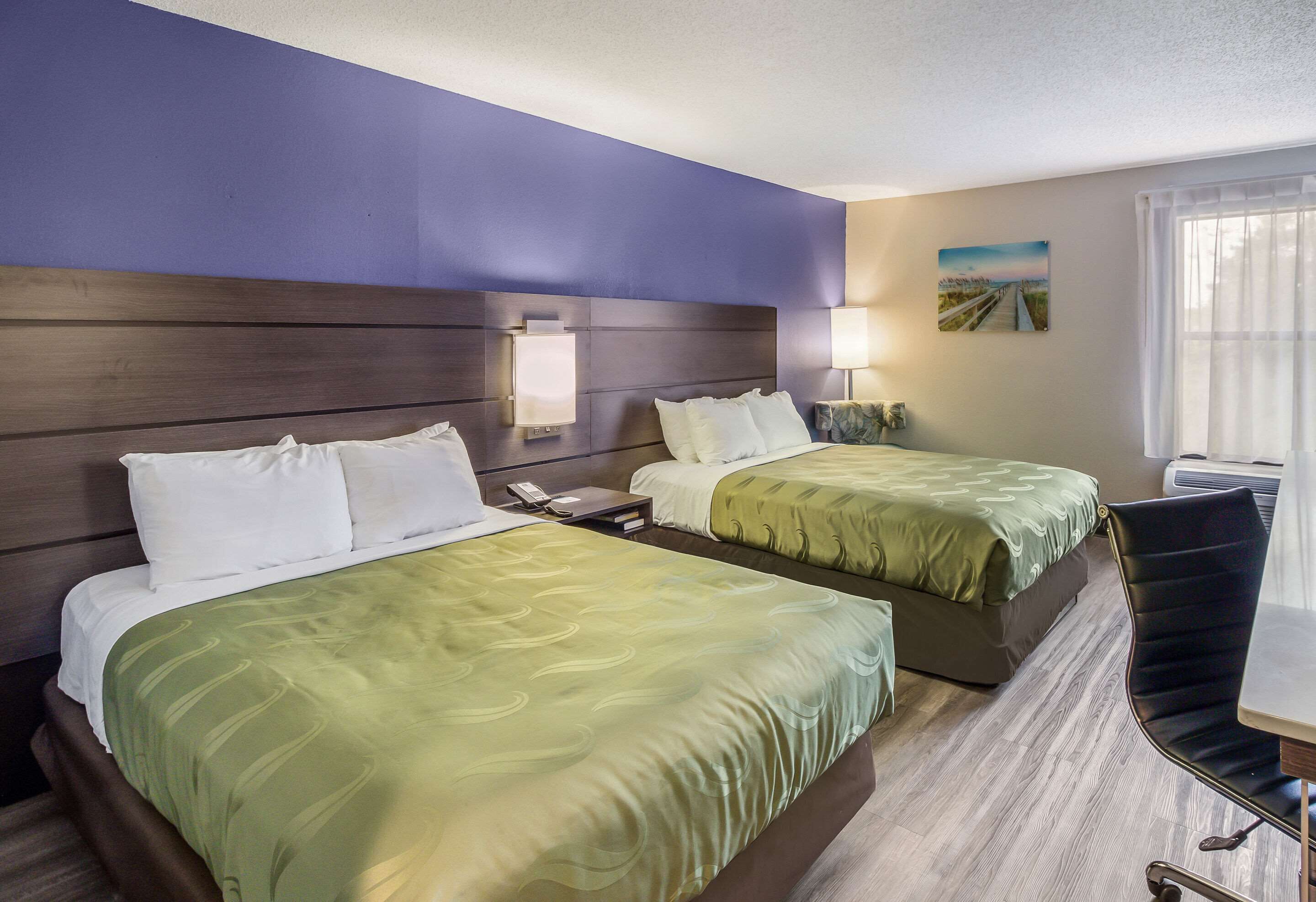 A hotel room with two beds, a desk, and a chair.