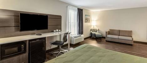 Habitación de hotel con cama, televisión, escritorio con computadora, una silla, sofá y ventana con cortinas.