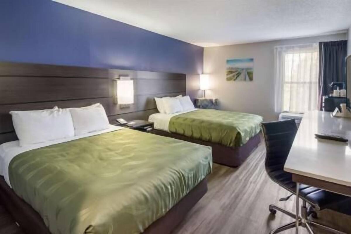 Une chambre d’hôtel avec deux lits, un bureau et une chaise.