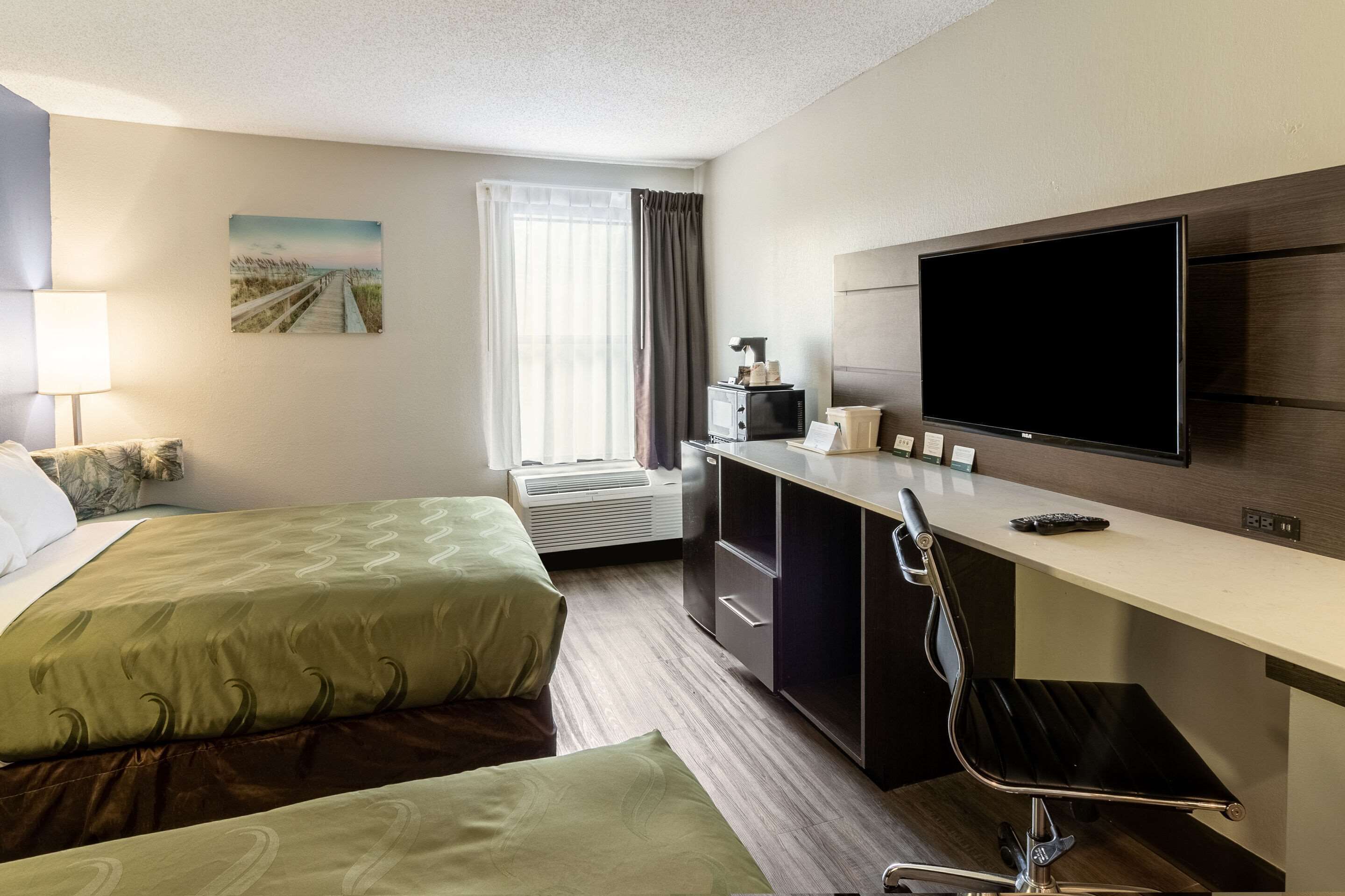 A hotel room with two beds, a desk, a TV, and a window with curtains.