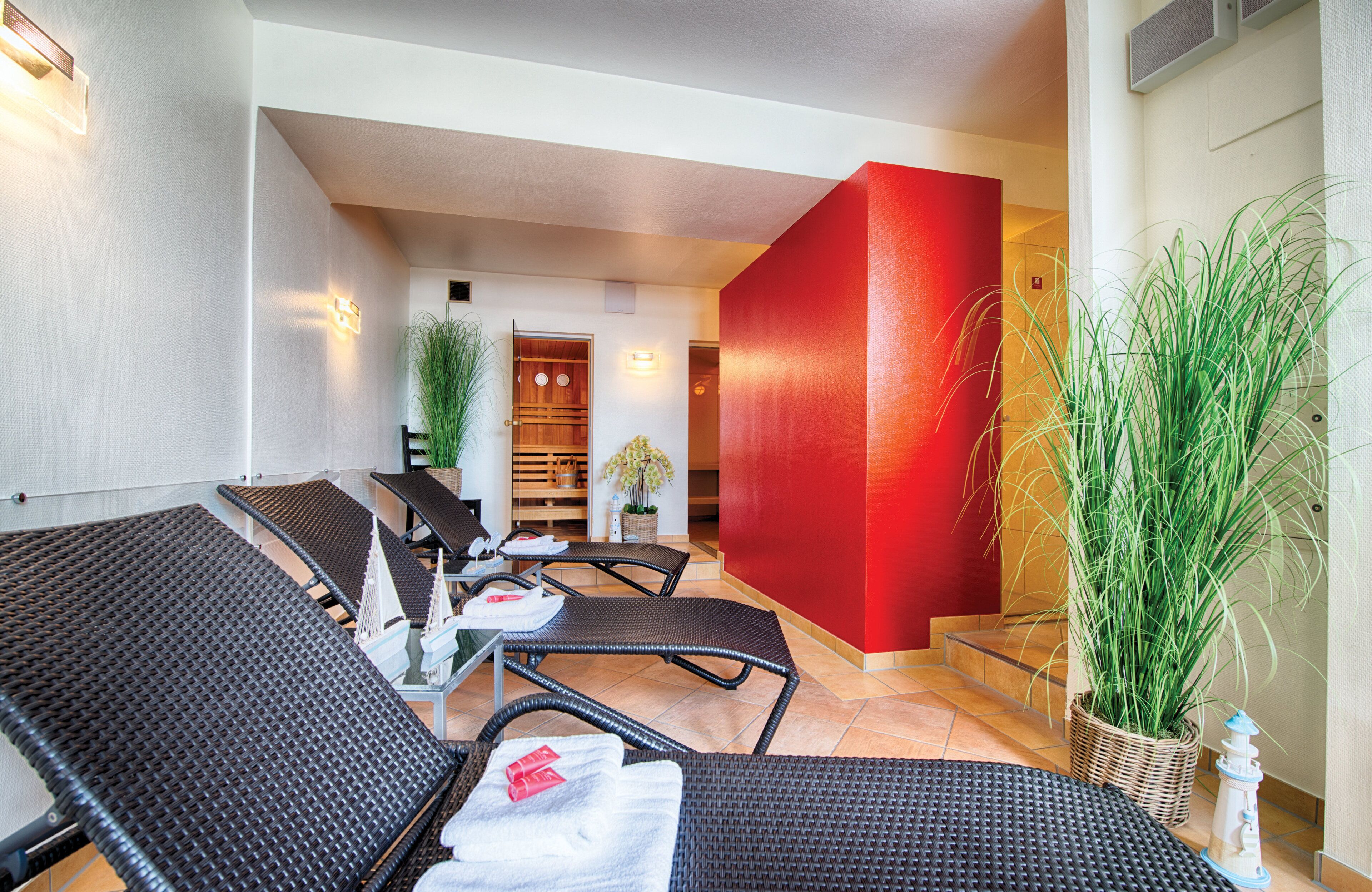 A hotel lobby with wicker lounge chairs, a red accent wall, and potted plants.