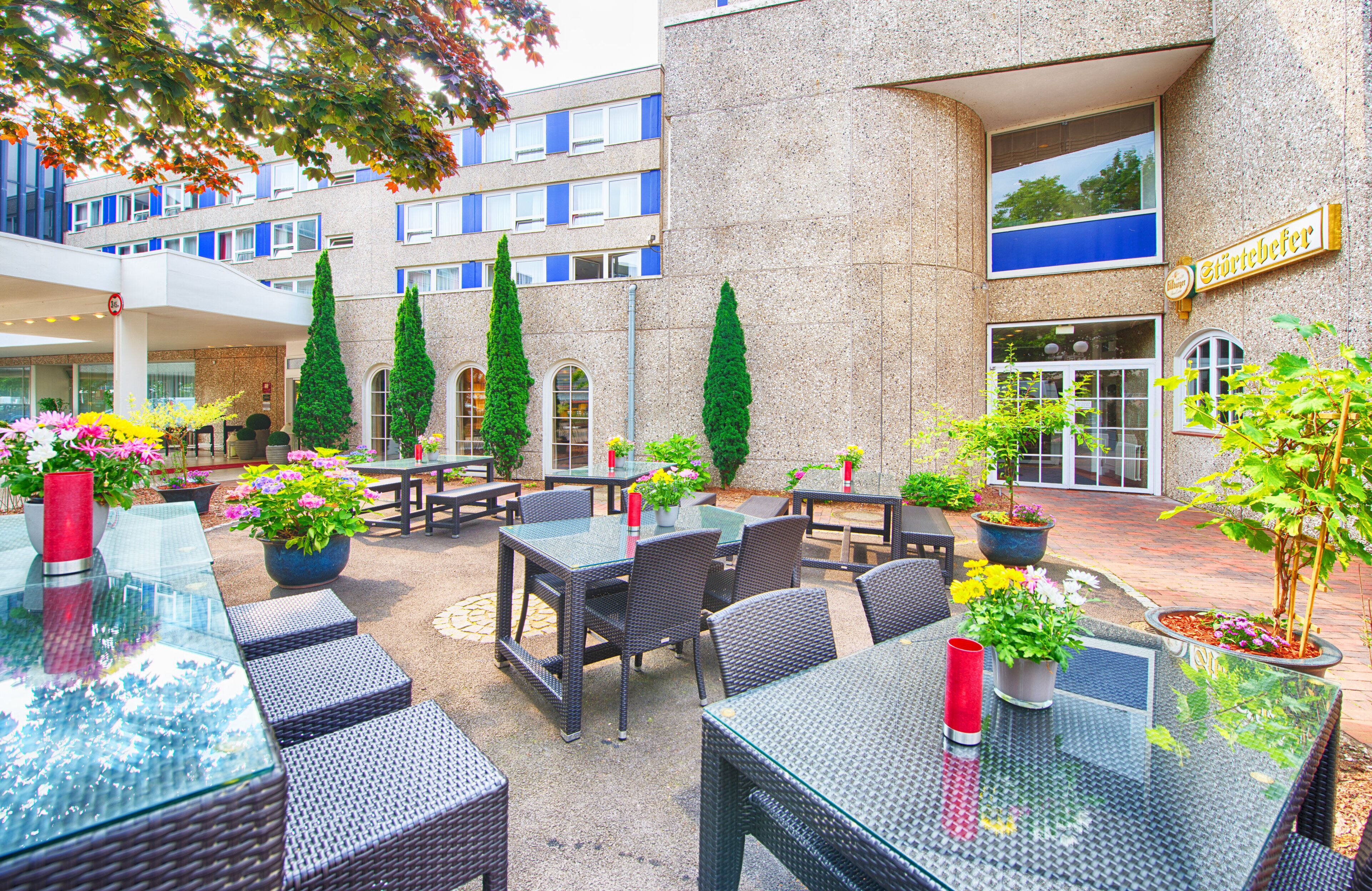 An outdoor seating area with tables and chairs, potted plants, and a building with a sign.