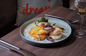 Un plato de comida sobre una mesa, junto a una copa de vino blanco y una cuchara.