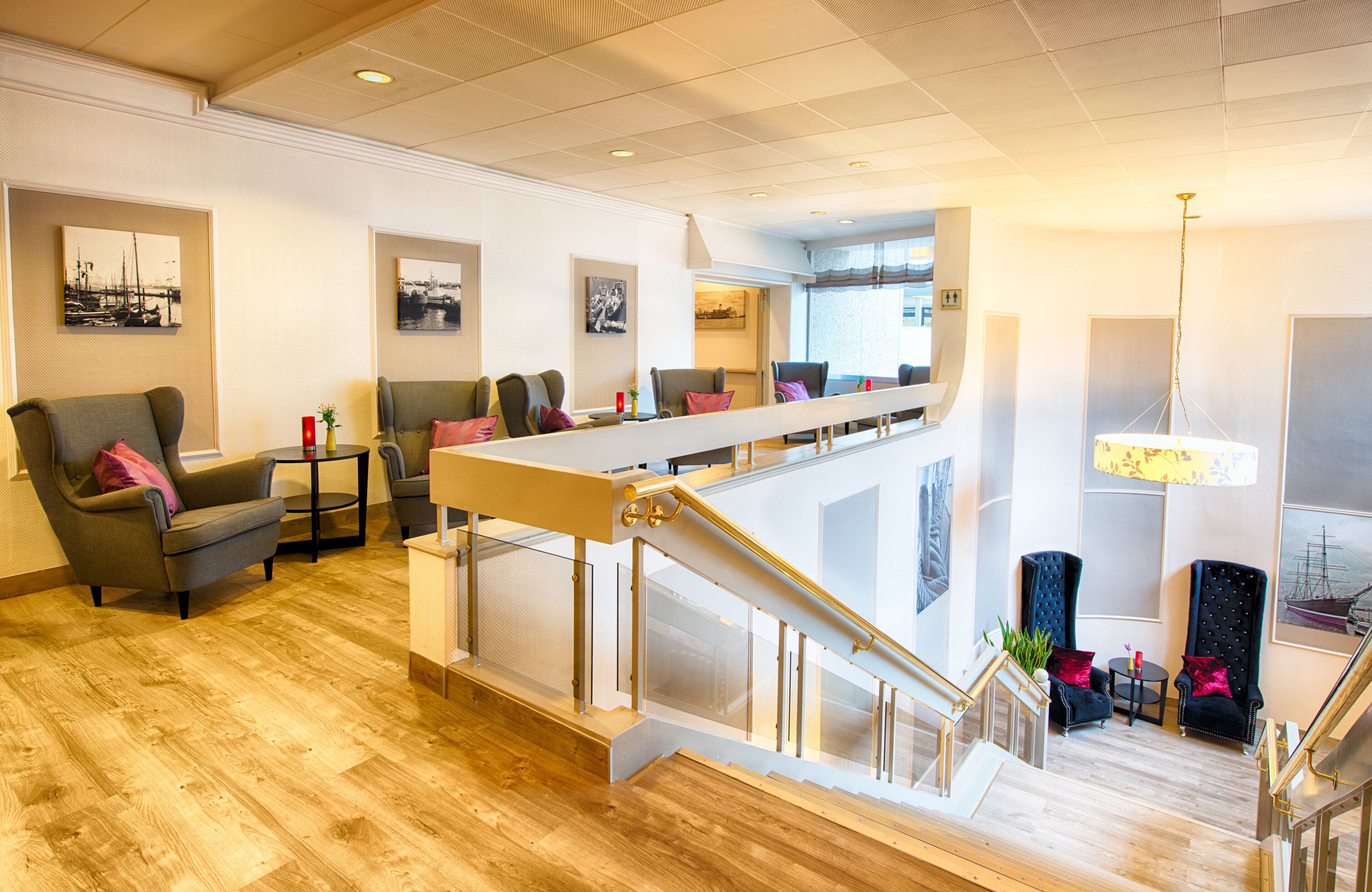Eine Hotelhalle mit Holzboden, einer Sitzecke mit Sofas, einer Treppe und Kunstwerken an den Wänden.